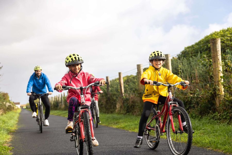 Twee kinderen op een rode fiets met een volwassene al fietsend in Ierland
